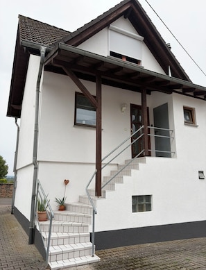 Un edificio de dos pisos con fachada blanca, una escalera de madera y un pequeño balcón.