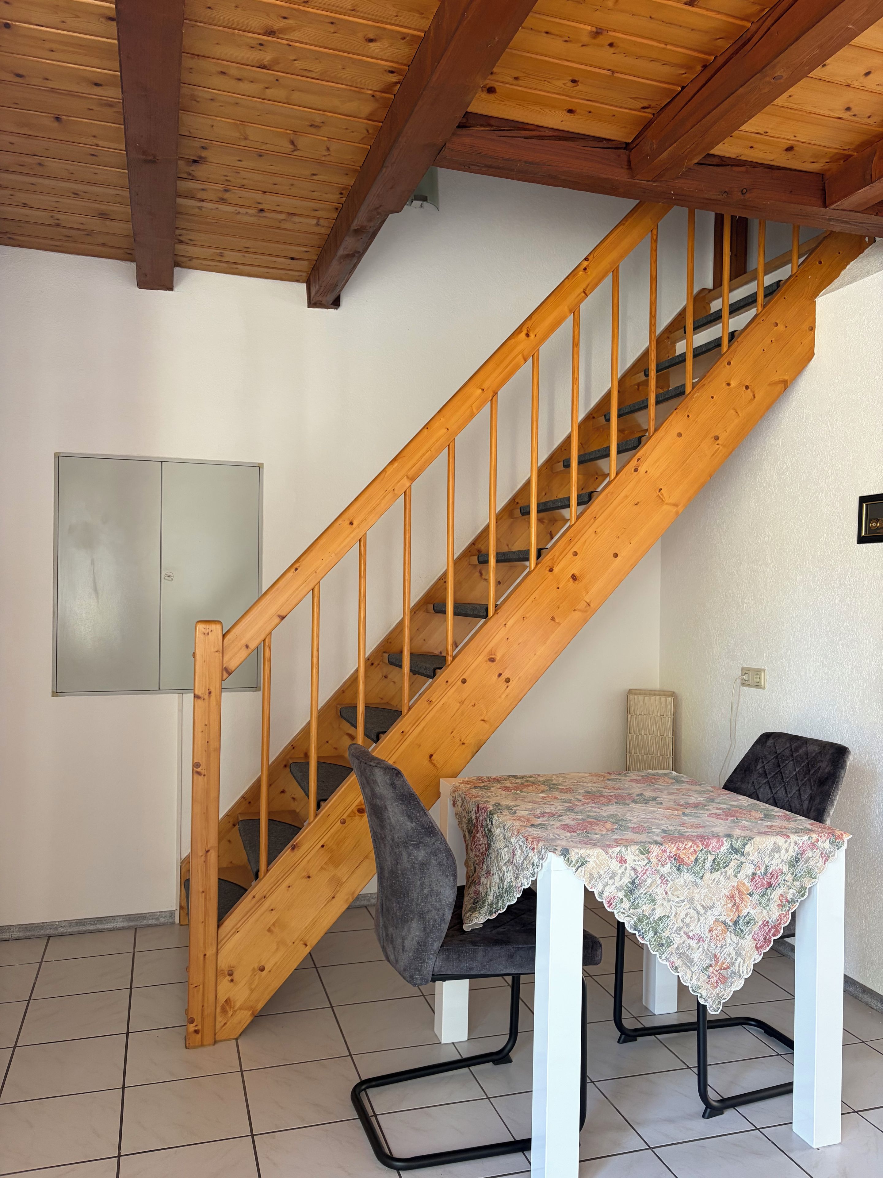 A wooden staircase with a chair and table in a room with tiled flooring.