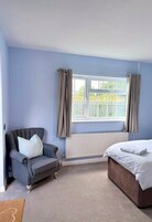 A bedroom with a bed, a chair, a window with curtains, and a radiator.