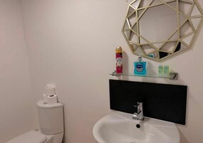 A bathroom with a white sink, a toilet, and a mirror with a geometric frame.