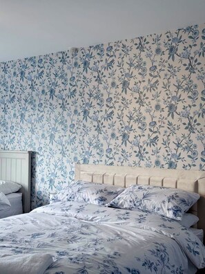 Quarto com papel de parede floral, cabeceira de madeira e cama com roupa de cama combinando.
