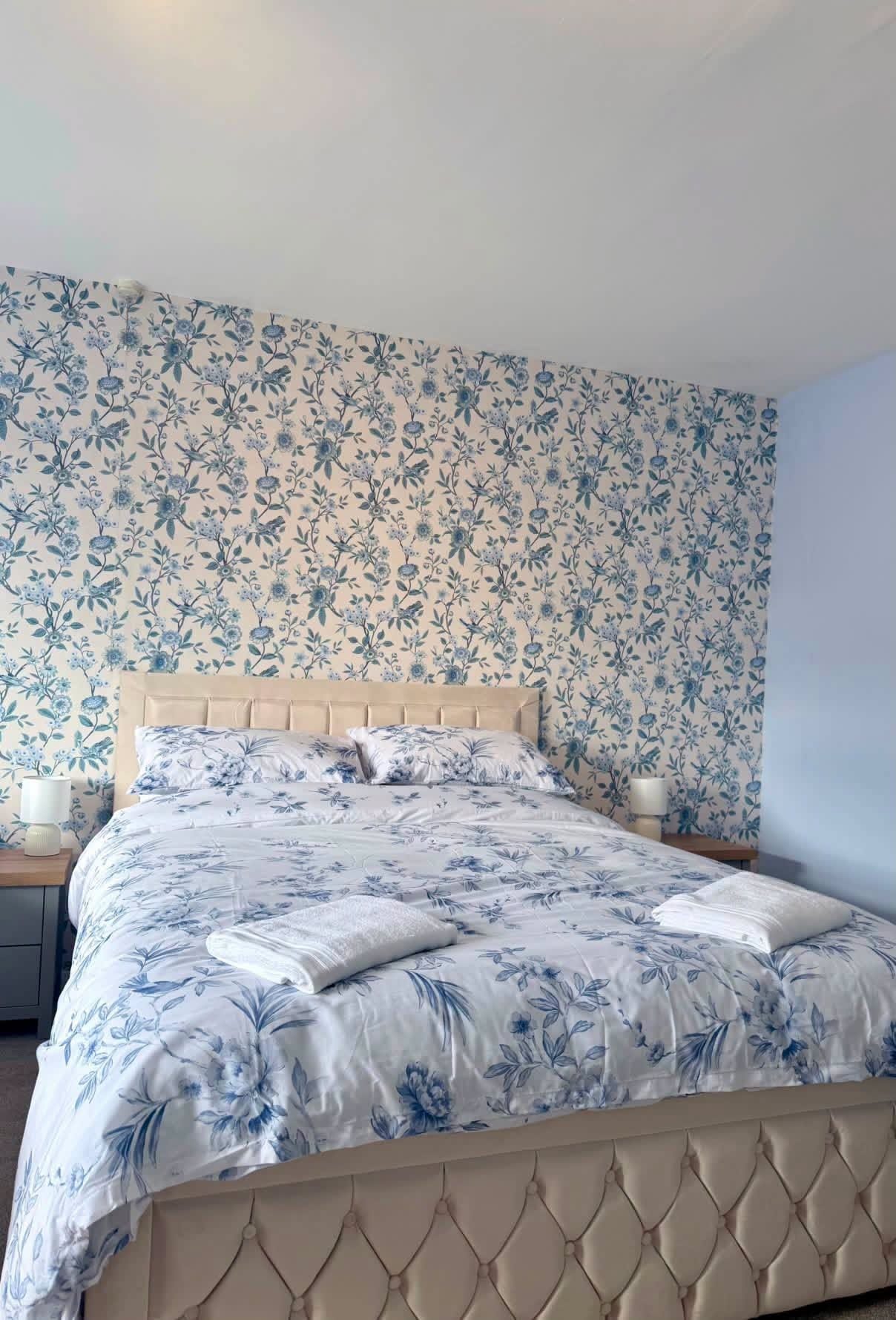 Un dormitorio con cama, papel tapiz floral y dos lámparas de noche.