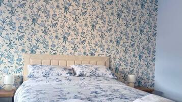 Un dormitorio con cama, papel tapiz floral y dos lámparas de noche.