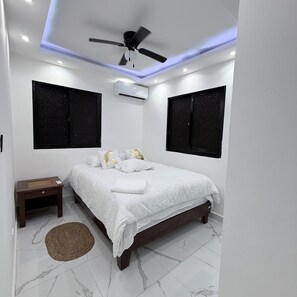 A bedroom with a bed, a nightstand, a ceiling fan, and an air conditioning unit. - Sunrise Ocean Views - Private Rooftop - BBQ - Near SDQ (Santo Domingo Este)