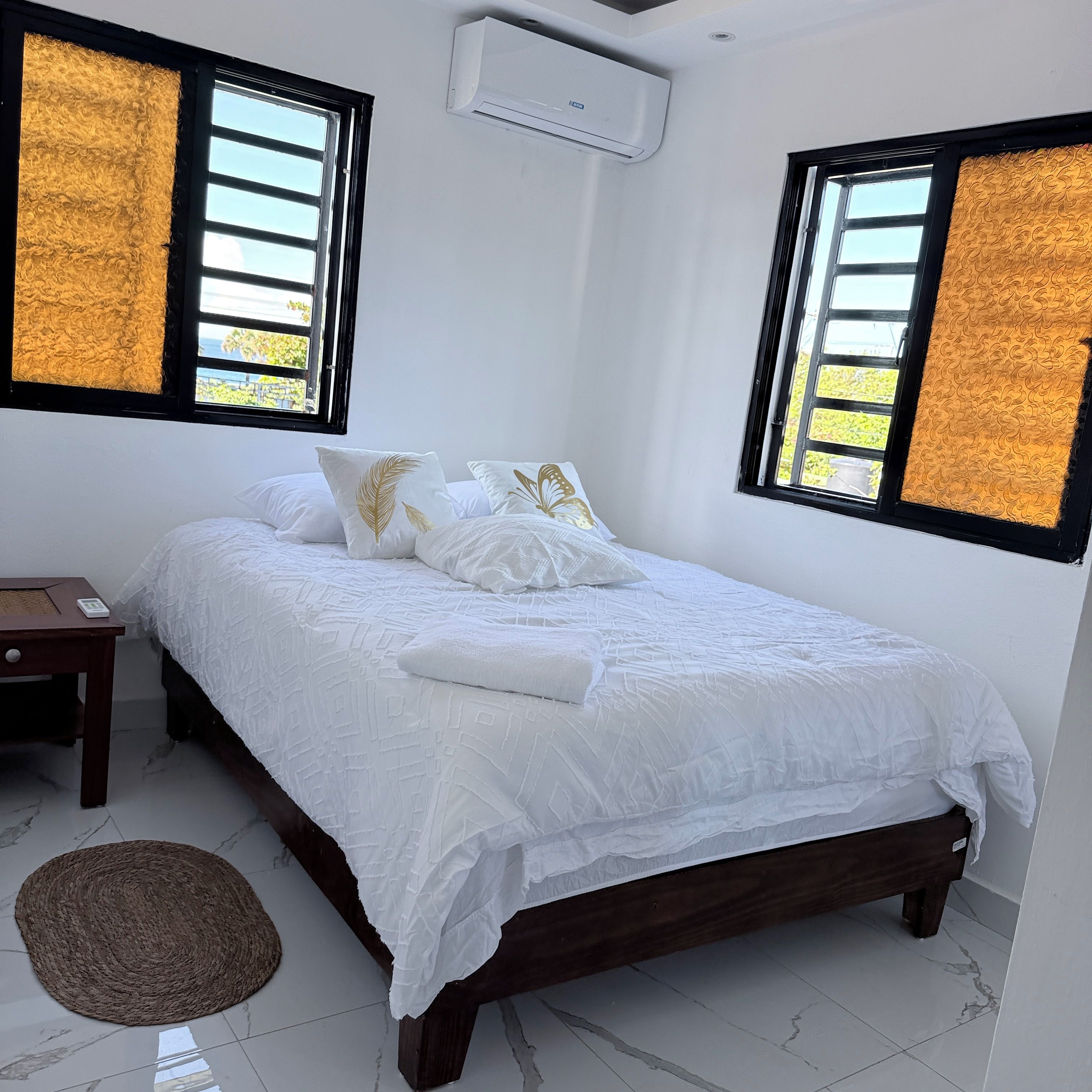 Une chambre à coucher comprenant un lit, des oreillers, une table de chevet, un appareil de climatisation et une fenêtre donnant sur un paysage agréable.