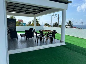 An outdoor patio with a grill, dining table, and chairs, overlooking a green lawn and a view of the sea. - Sunrise Ocean Views - Private Rooftop - BBQ - Near SDQ (Santo Domingo Este)