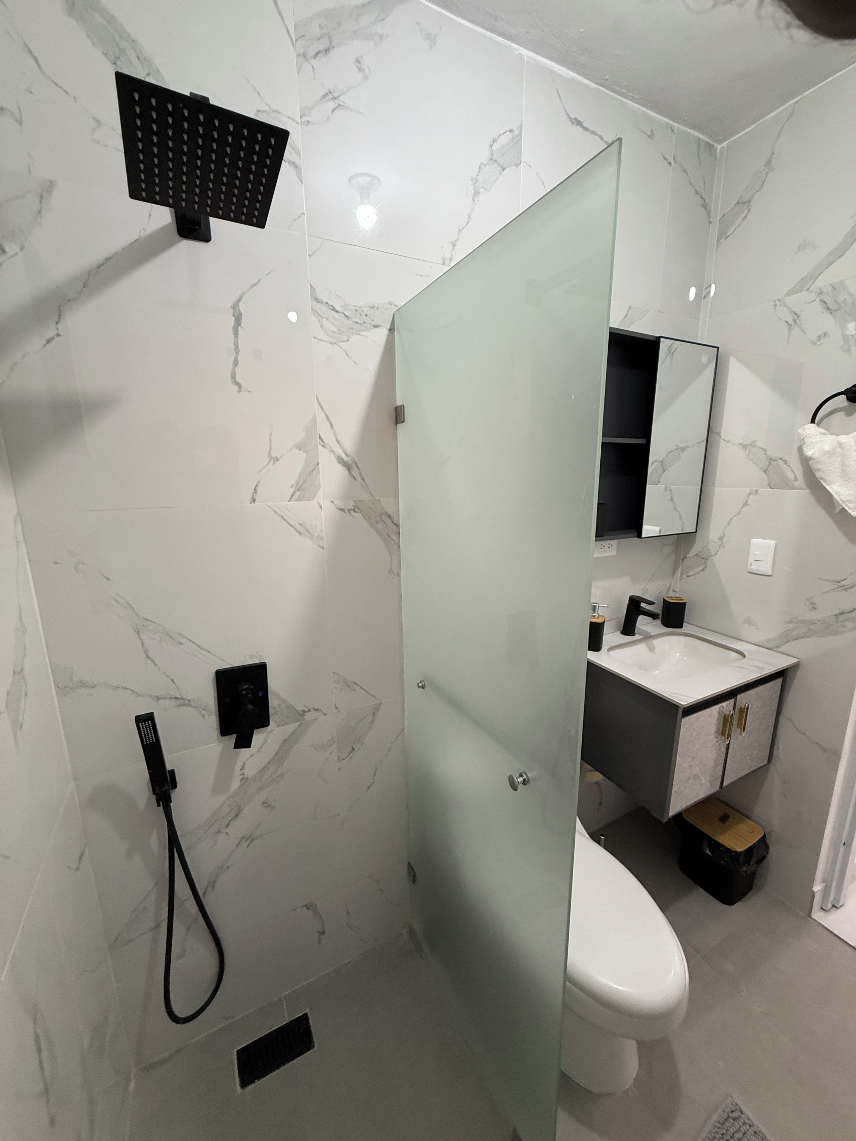 Une salle de bain avec une douche à parois de verre, un lavabo avec un miroir et des toilettes.
