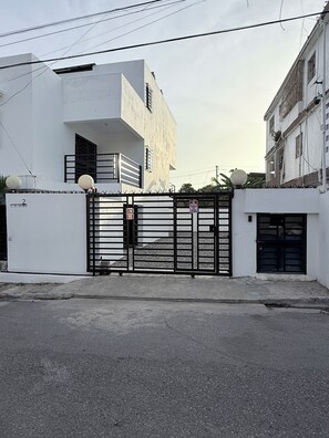 A gated entrance to a building with a modern architectural style, featuring a flat facade and a large, black metal gate. - Sunrise Ocean Views - Private Rooftop - BBQ - Near SDQ (Santo Domingo Este)