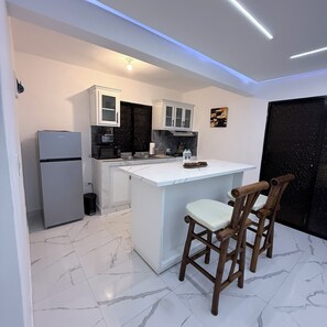 A modern kitchen with white cabinets, a built-in island, and a refrigerator.
