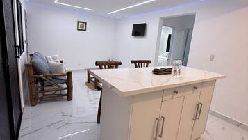 Une cuisine moderne avec un plan de travail en marbre, des chaises en bois et un téléviseur encastré.