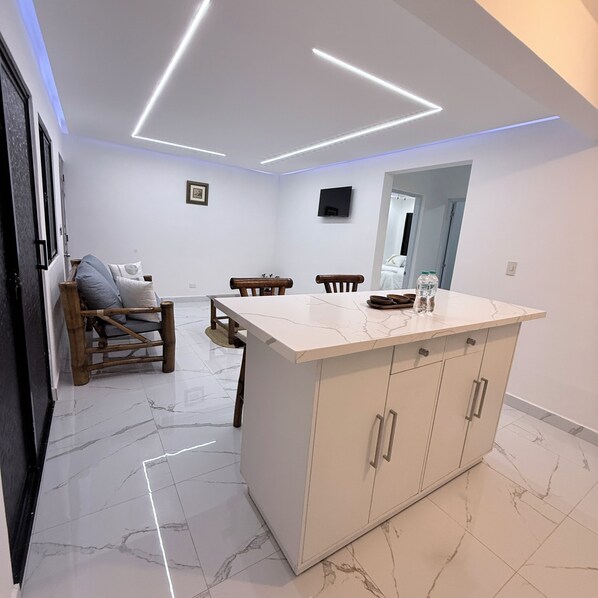 A modern kitchen with a marble countertop, wooden chairs, and a built-in TV.