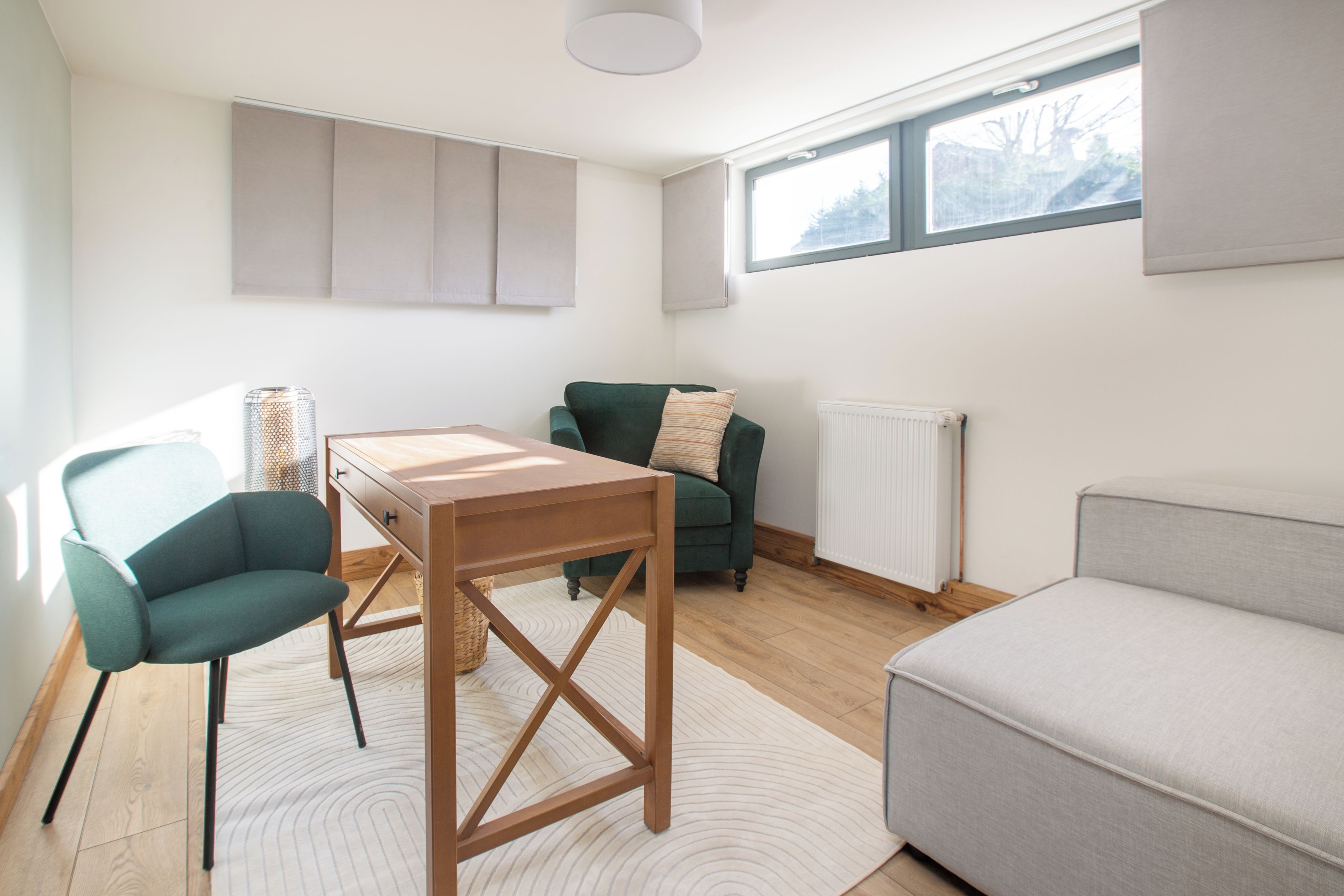 Een moderne woonkamer met een houten salontafel, een groene fauteuil, een grijze bank en een radiator.