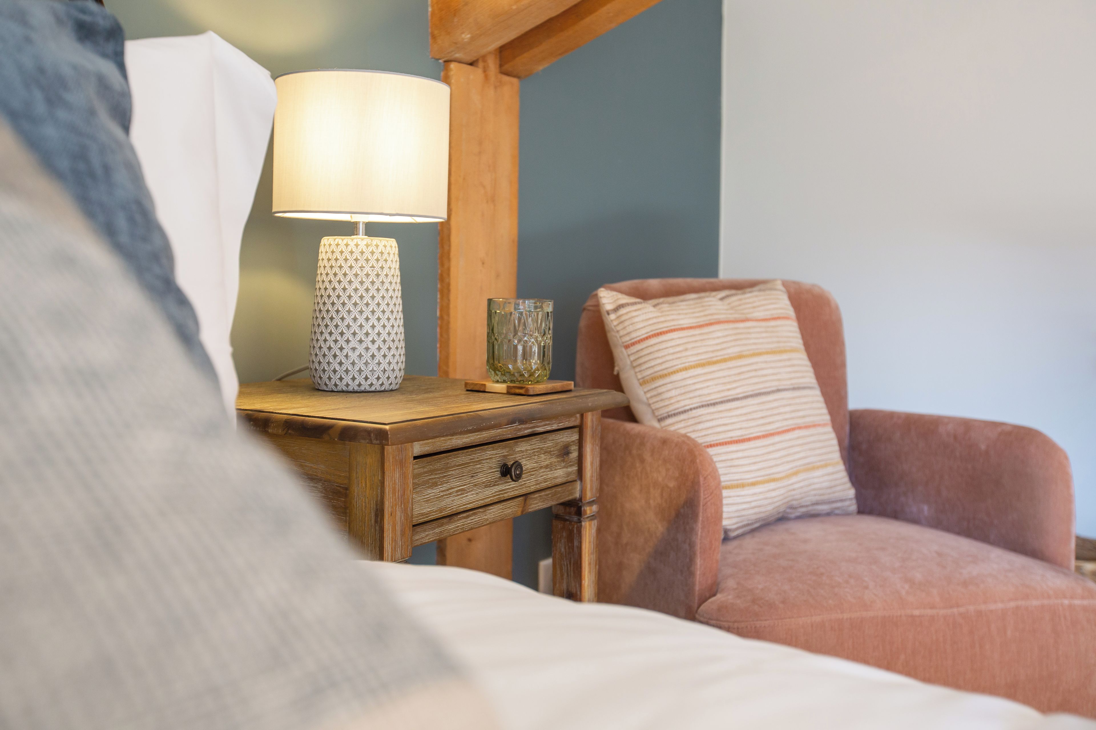 Een slaapkamer met een houten nachtkastje, een lamp, een glas en een gestreept kussen.