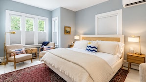 A bedroom with a large bed, two bedside tables, a chair, a window with blinds, and a rug. - Sea Spray
Charming Three Bedroom House with amazing views of Camden Harbor (Camden)