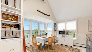A spacious kitchen with white cabinetry, a dining area with a table and chairs, and a large window offering a view. - Sea Spray
Charming Three Bedroom House with amazing views of Camden Harbor (Camden)
