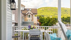 A porch with a white railing, a table, and two chairs. There is a black lantern on the wall. The view includes a house and a green hill. - Sea Spray
Charming Three Bedroom House with amazing views of Camden Harbor (Camden)