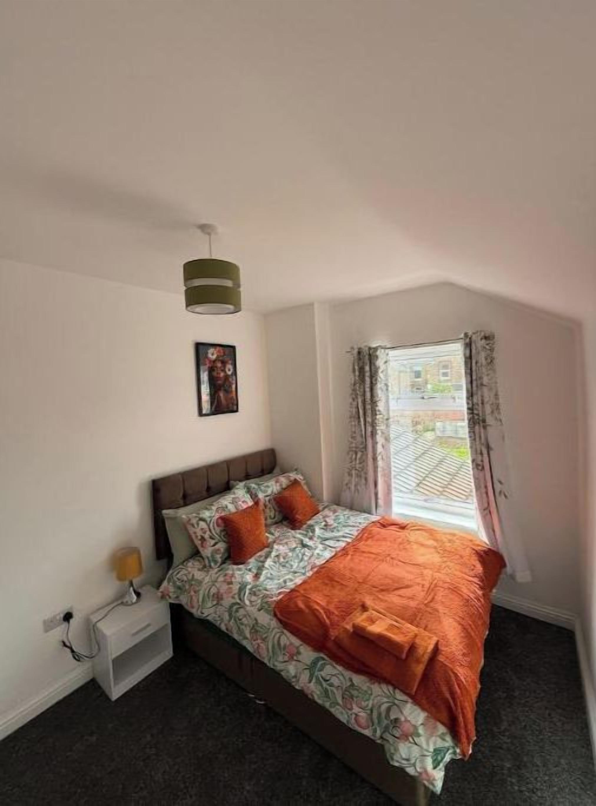 A bedroom with a bed, a nightstand, a lamp, a window with curtains, and a picture on the wall.