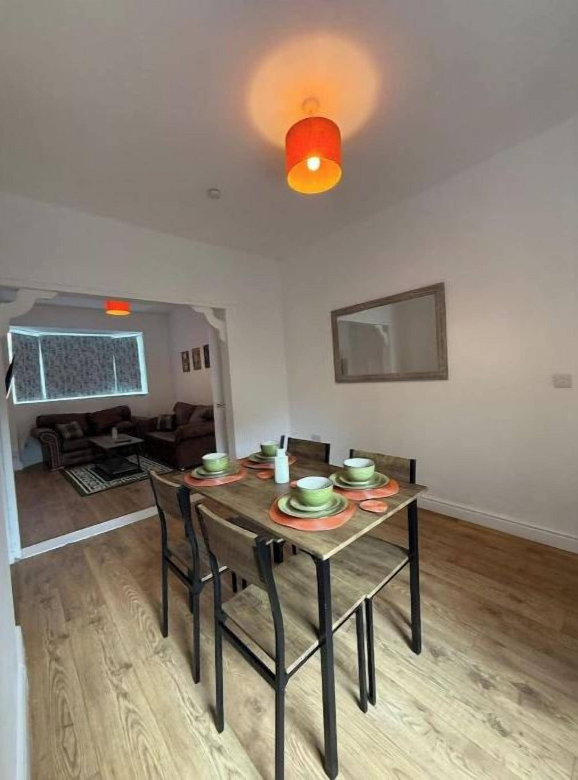 Un coin repas avec une table dressée pour quatre personnes, un plancher en bois, un luminaire au plafond et un tableau encadré accroché au mur.