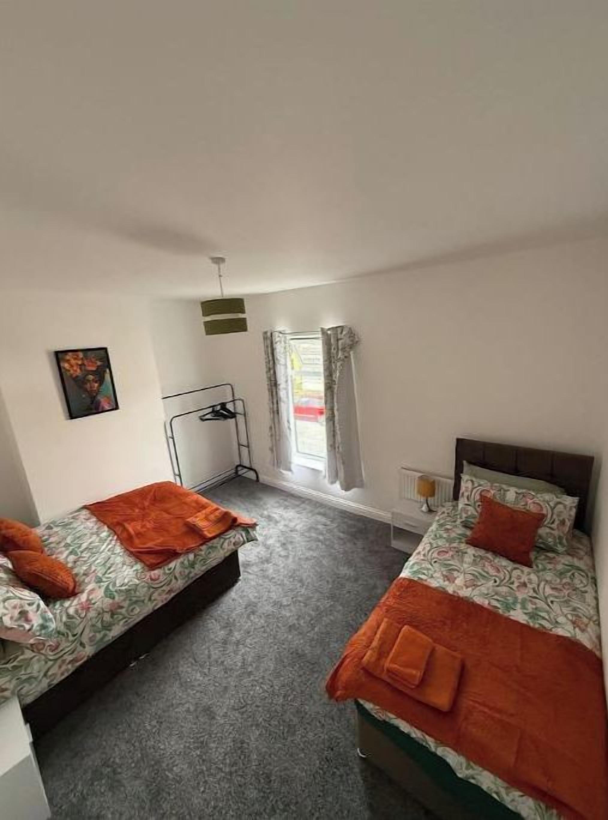 Een kamer met twee bedden, een radiator, een raam met gordijnen en een aan de muur hangend schilderij.