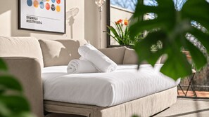 A bed with white linens and rolled towels, a beige sofa, and a framed picture on the wall. - Turner & Tonic at Avron City Escape (Turner)