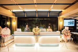 A reception desk with two staff members, a large window with blinds, and a screen displaying a message. - ATSINI Pererenan (Pererenan)