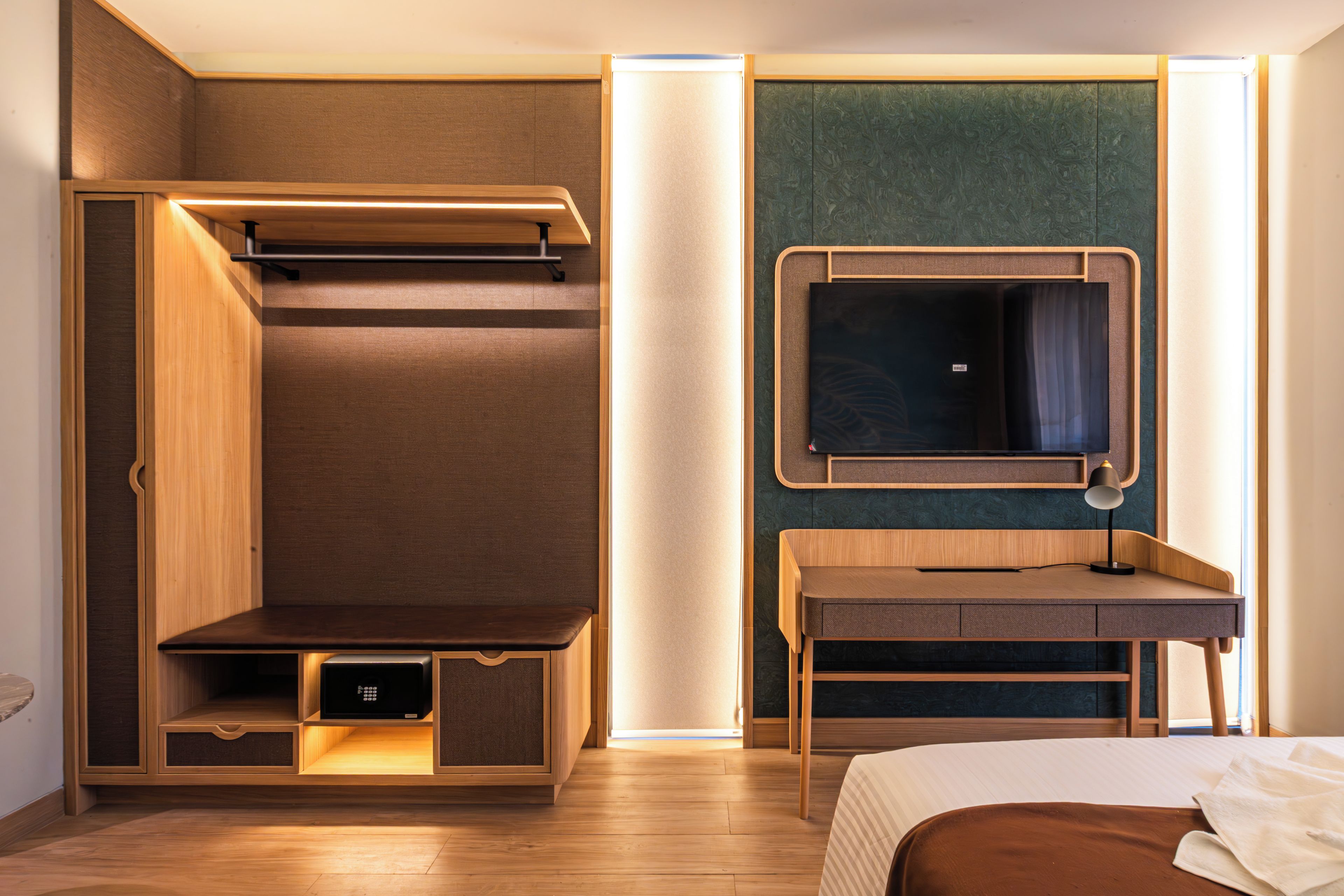 A modern hotel room with a bed, a desk, a built-in wardrobe, and a mirror.