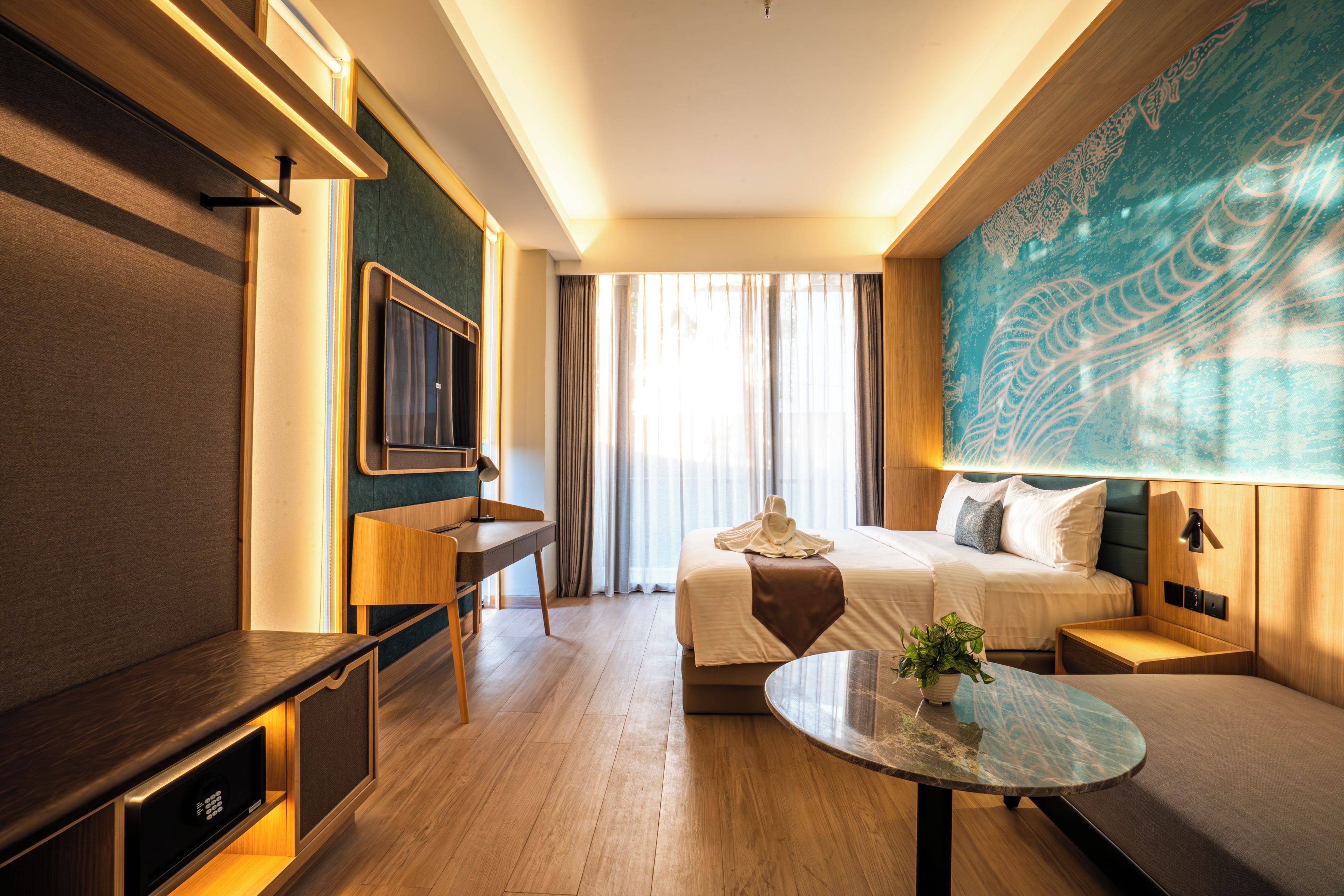Een hotelkamer met een bed, een bureau, een televisie, een groot raam met gordijnen en een wand met een decoratief patroon.
