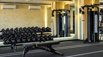 Un gimnasio con equipo de levantamiento de pesas, incluyendo mancuernas y una prensa de banca.