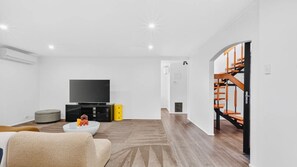 Ein modernes Wohnzimmer mit Flachbildfernseher, Couchtisch und einer Treppe, die zu einer oberen Ebene führt.