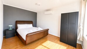 A neatly made bed with white linens and a brown headboard in a room with wooden flooring. - Adinda & Co. A Canberra Family Stay (Waramanga)