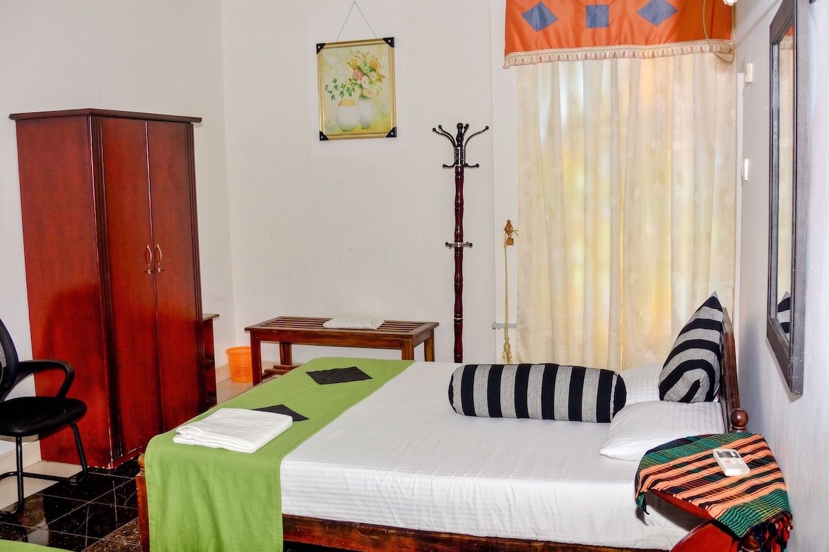Quarto de hotel com cama, guarda-roupa de madeira, escrivaninha, cadeira e janela com cortinas.