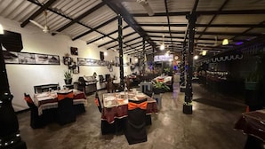 Amplo espaço interno com mesas preparadas para refeições, área de bar e teto com vigas aparentes.