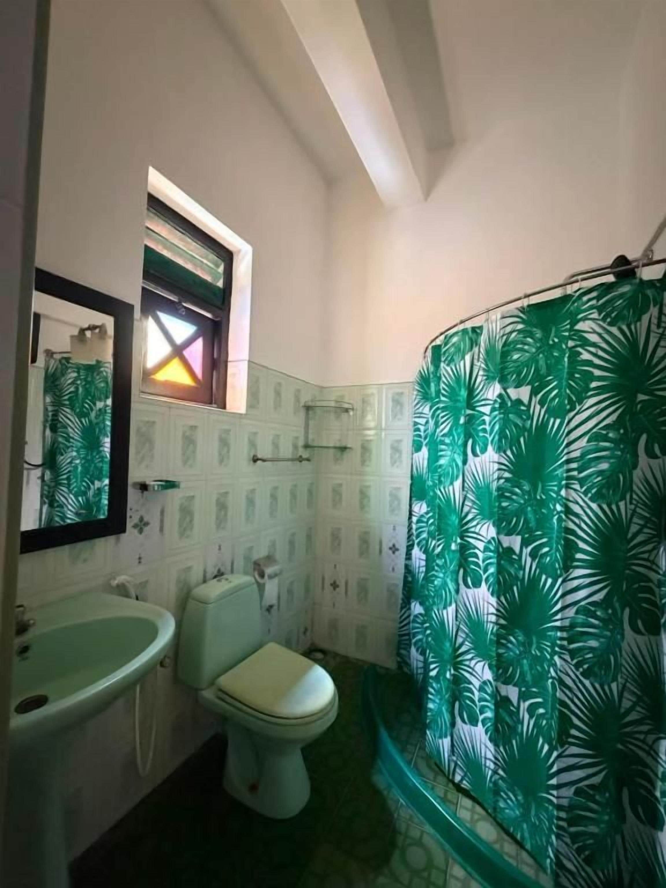 Une salle de bain équipée de toilettes, d’un lavabo et d’un rideau de douche orné d’un motif de feuilles.