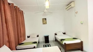 Quarto de hotel com duas camas de solteiro, ventoinha no teto, ar condicionado e uma mesinha.