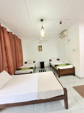 Een hotelkamer met twee eenpersoonsbedden, een plafondventilator, een airconditioner en een klein tafeltje.