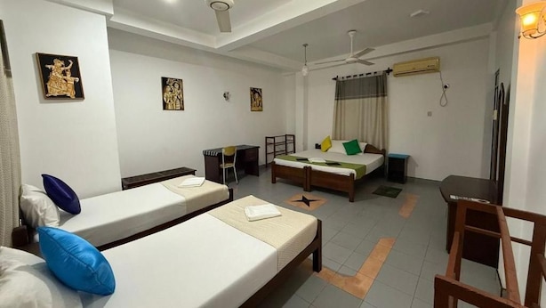 Quarto de hotel com duas camas de solteiro, uma escrivaninha, uma cadeira e um ventilador de teto.