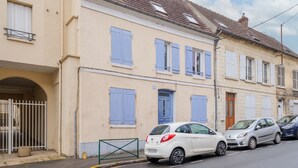 Eine Wohnstraße mit einer Reihe von zweigeschossigen Häusern, jedes mit einem Balkon und einem kleinen Fenster. Autos sind entlang der Straße geparkt.