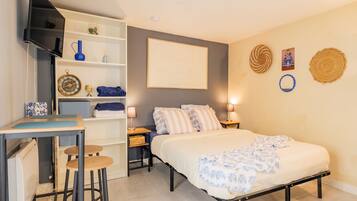 Een slaapkamer met een bed, een bureau, een stoel, een televisie en een plank met decoratieve objecten.