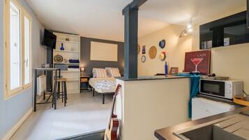 Een knus woongedeelte met een kitchenette, een bed met gestreepte lakens, een gitaar en een tv aan de muur.