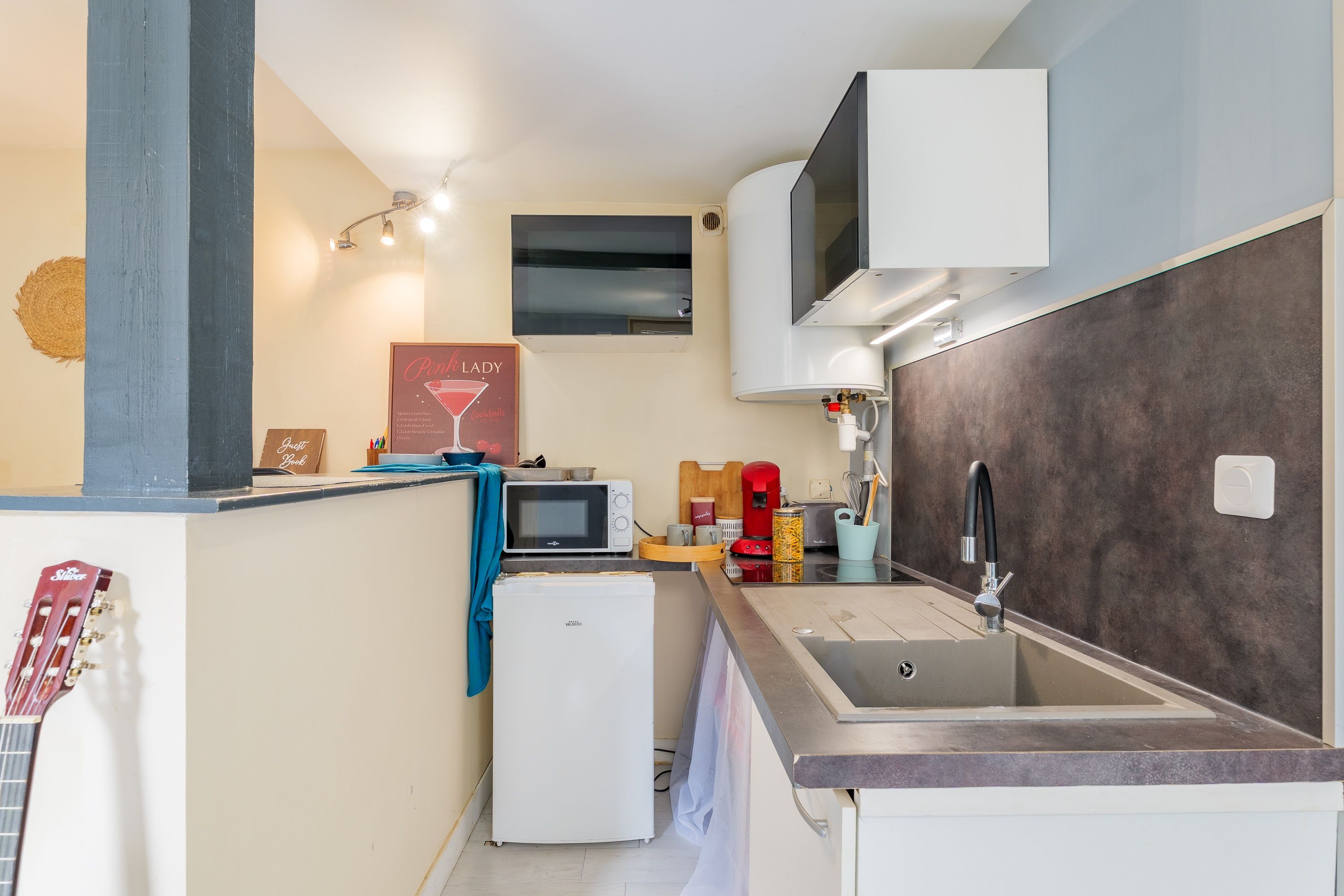 Een compacte keuken met een ingebouwde magnetron, een kleine koelkast, een wastafel met een moderne kraan en een wandairconditioner.