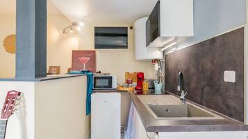 Een compacte keuken met een ingebouwde magnetron, een kleine koelkast, een wastafel met een moderne kraan en een wandairconditioner.