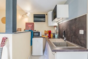 Une cuisine compacte équipée d’un micro-ondes encastré, d’un petit réfrigérateur, d’un évier avec un robinet moderne et d’un climatiseur fixé au mur.