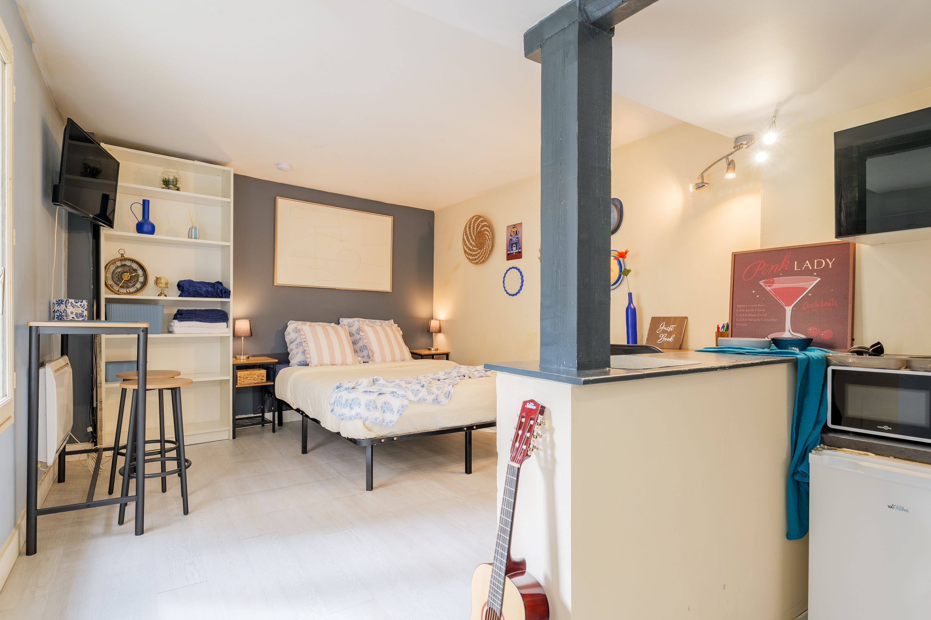 Une chambre à coucher de taille modeste, comprenant un lit, des tables de chevet, un bureau et une guitare.