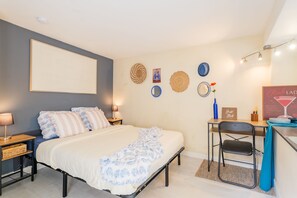 Une chambre à coucher comprenant un lit, des tables de chevet, un bureau avec une chaise, une étagère fixée au mur et une horloge murale.