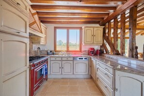 A kitchen with a red stove, white cabinets, and a large window. - Maison du Chemin des Vignes - charme normand (L'Oudon)