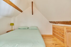 Una camera da letto con soffitto spiovente, un letto con due cuscini, un comodino con una lampada e travi in legno.