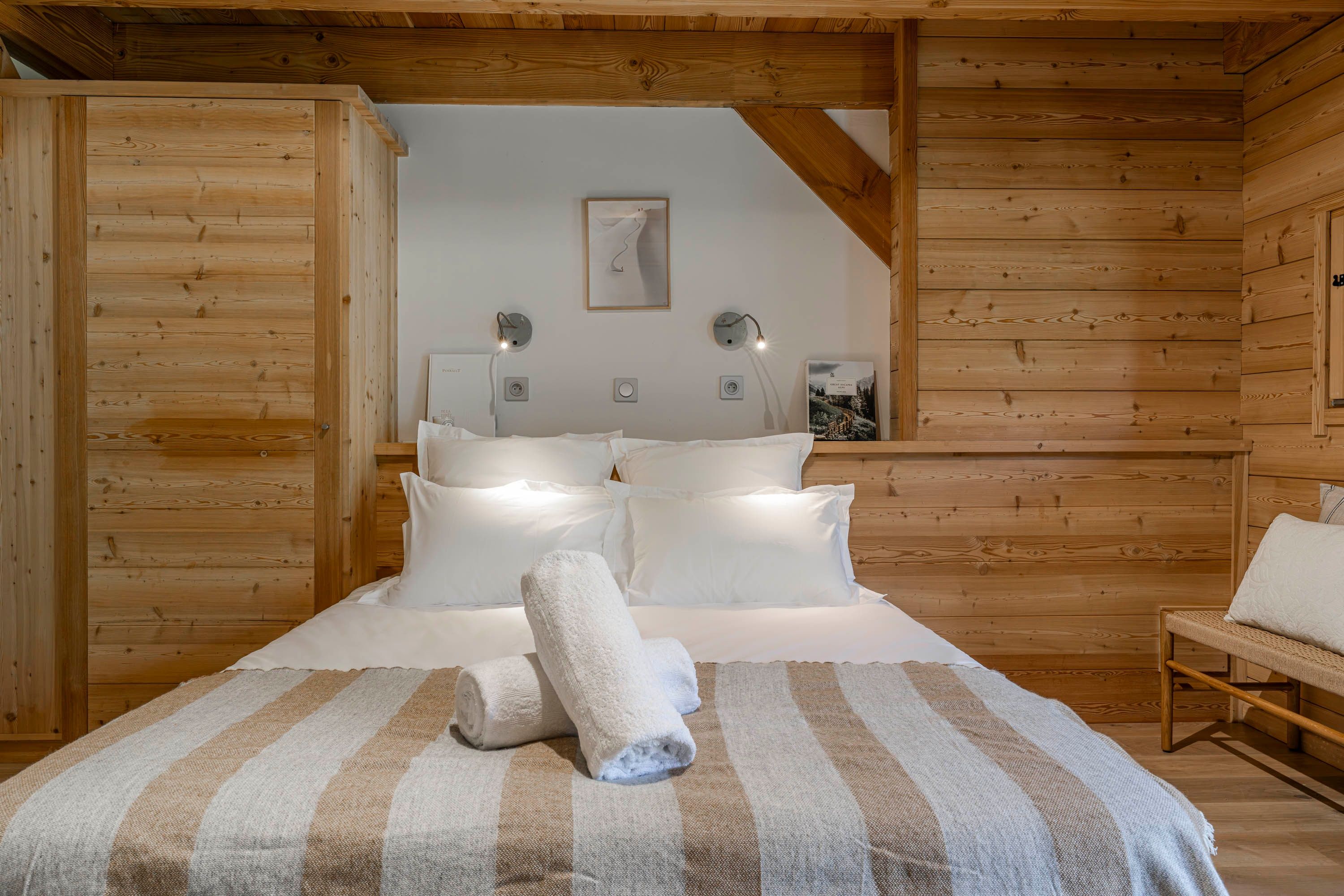 Ein gemütliches Schlafzimmer mit Holzbalkendecke, einem Bett mit weißen Leinen und zwei Wandlampen.