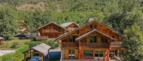 A wooden cabin with a covered carport, a patio with outdoor seating, and a view of a mountainous landscape.