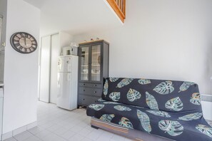 Ein kompakter Wohnraum mit einer Couch, einem Schrank, einem Kühlschrank und einer Wanduhr.