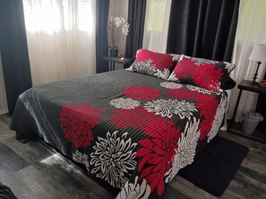 A bed with a floral-patterned bedspread, a bedside table with a lamp, and a window with sheer curtains. - Wonderful 3-bedroom house with AC in charming Kailua (Kailua)